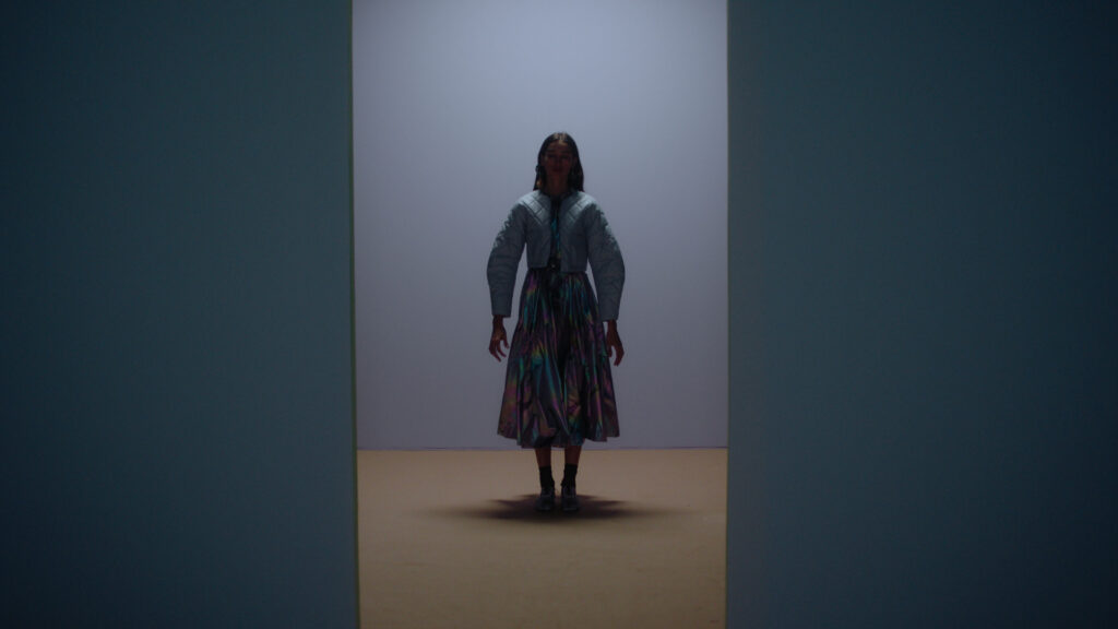Color Grading example. Latin woman dressed in light blue in twilight. In light blue room with light brown floor. Overhead lighting from behind.