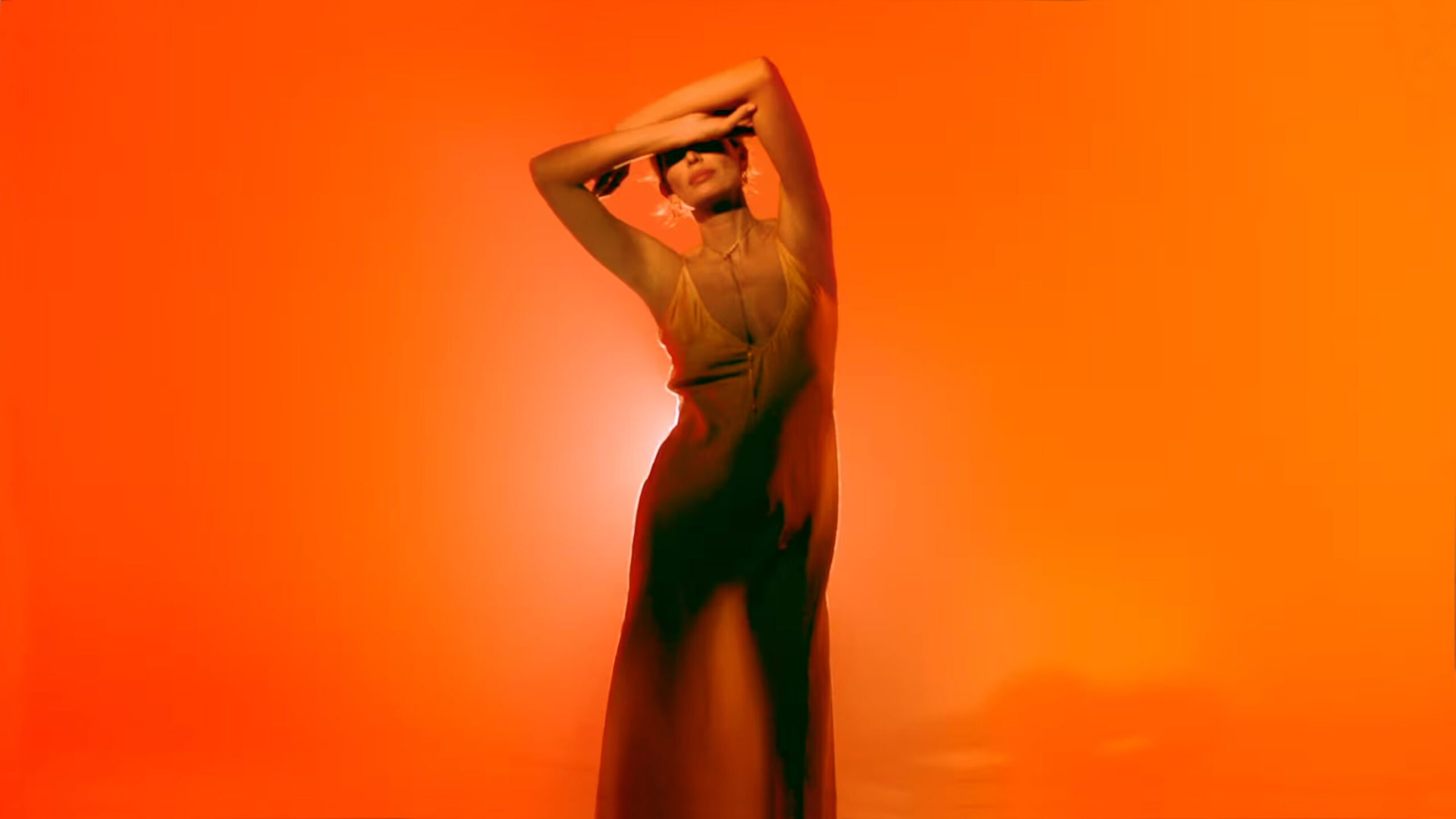 Still from a perfumery advertisement as an example of the use of color. Woman with skin-colored dress, on orange background illuminated by warm light.