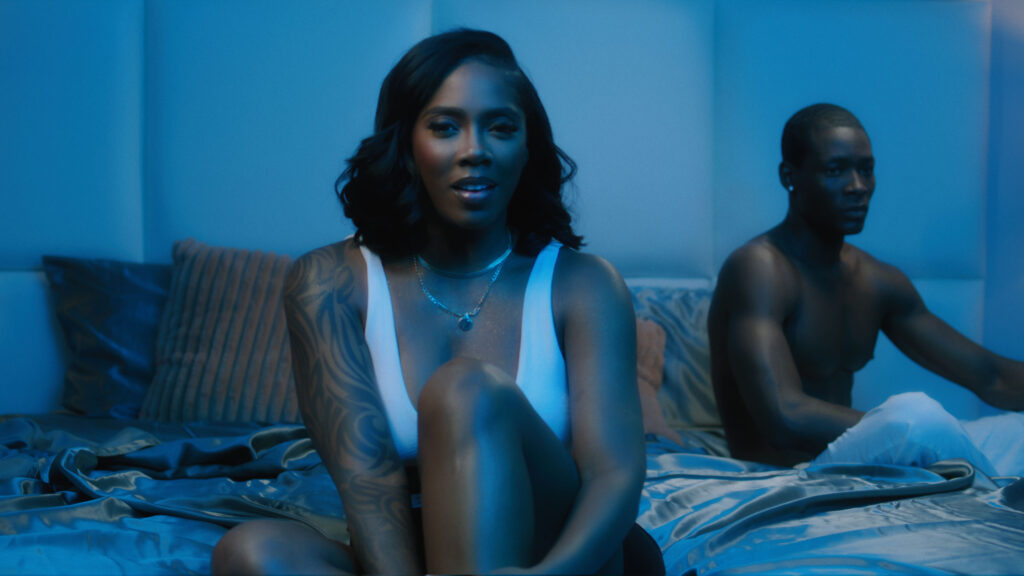 Still from a music video as an example of the use of color. Black woman on brown bed, illuminated by warm and blue light.